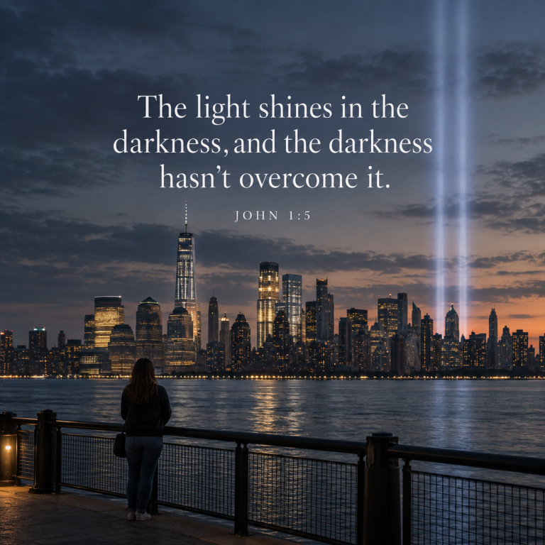A woman stands quietly overlooking Lower Manhattan as the Tribute in Light rises into the evening sky, with John 1:5 displayed: “The light shines in the darkness, and the darkness hasn’t overcome it.”